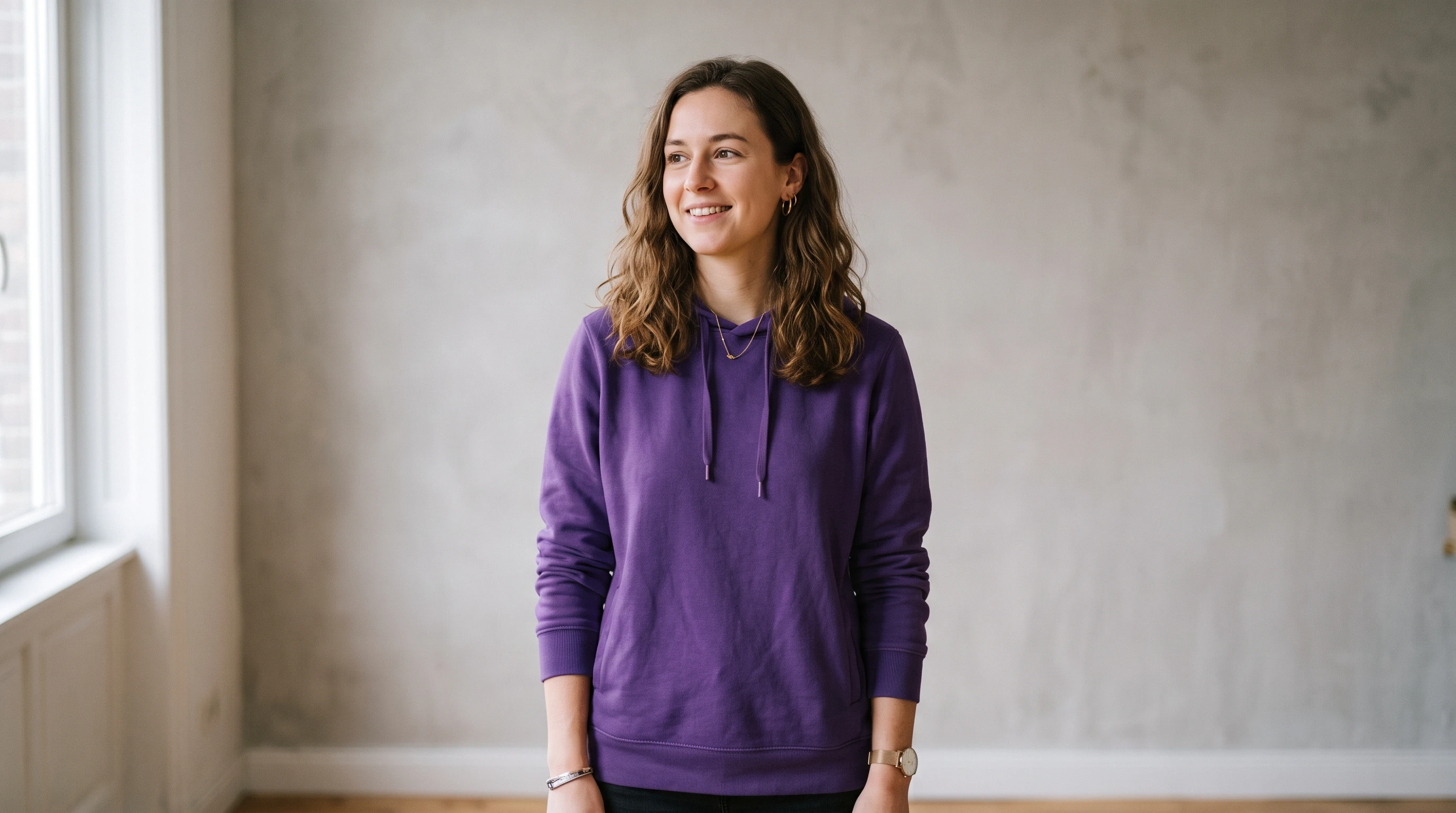 A person wearing a plain purple hoodie against a light grey wall